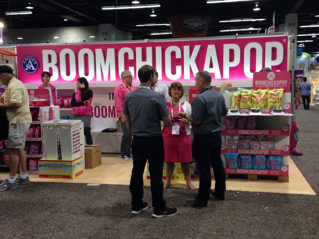A busy trade show booth, with several people in the booth space and aisle, talking.